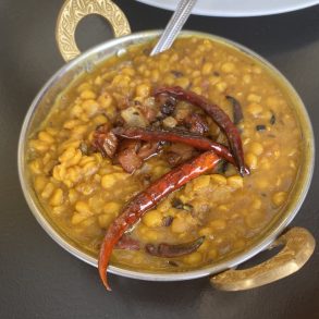 A bowl of yellow curry with red peppers and a spoon.